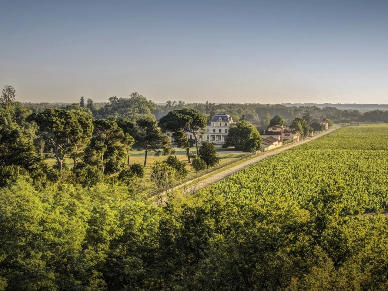 Aerial view of Château Giscours near Bordeaux, featuring its white neoclassical manor house surrounded by lush vineyards and forests in the Médoc region.