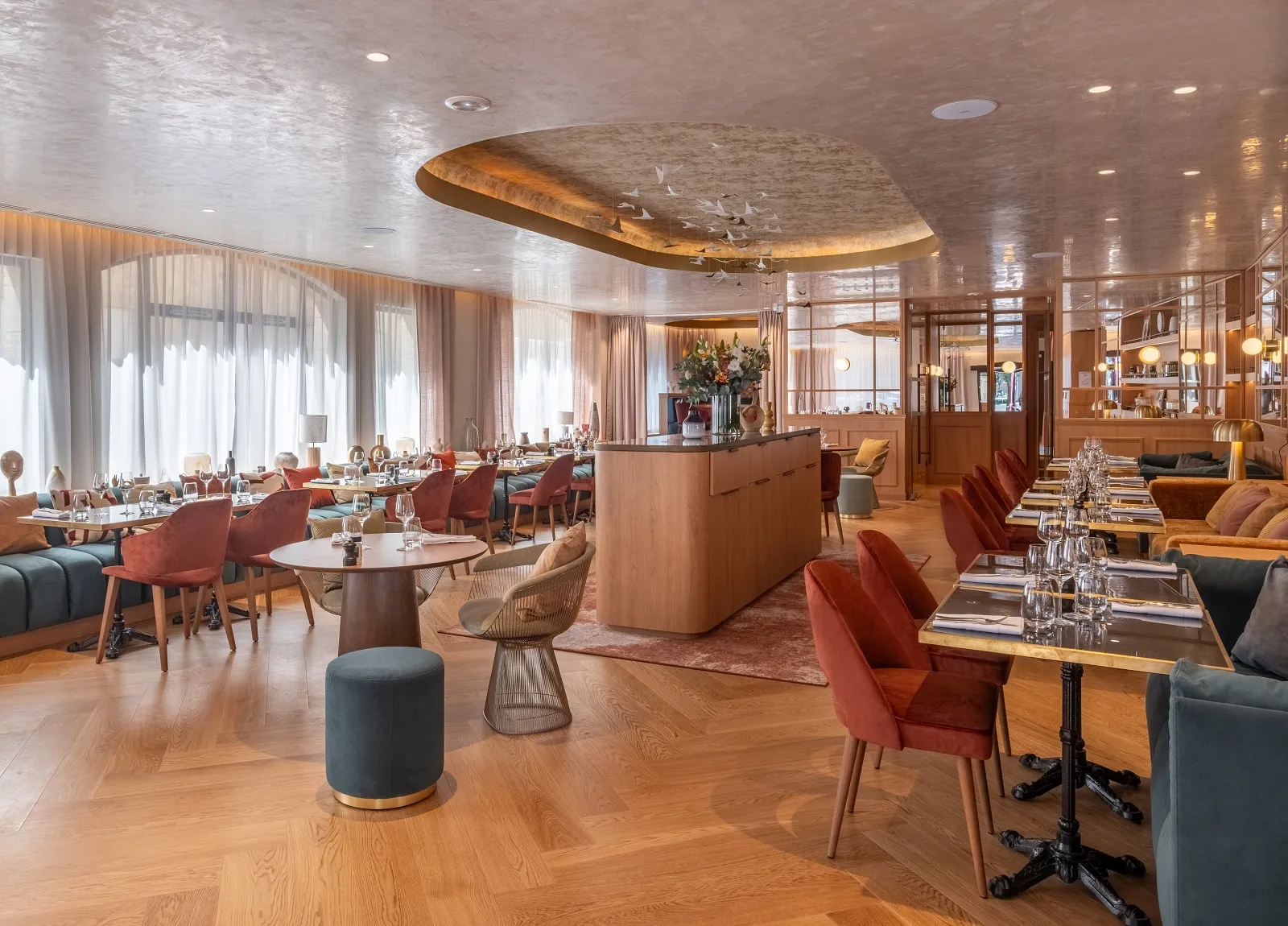 Elegant restaurant at Madame B in Bordeaux featuring red chairs, round tables, glossy white ceiling, large bay windows, and light wood modern furniture