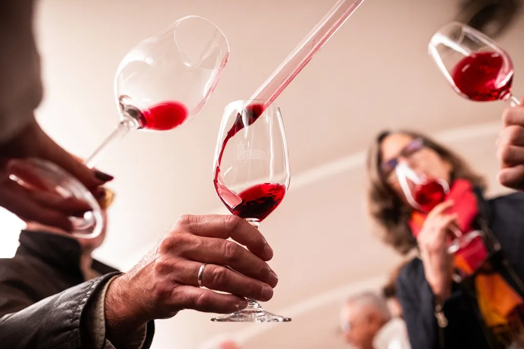 Group of people holding glasses of red wine during a tasting in Bordeaux, with wine being poured into a glass in the foreground