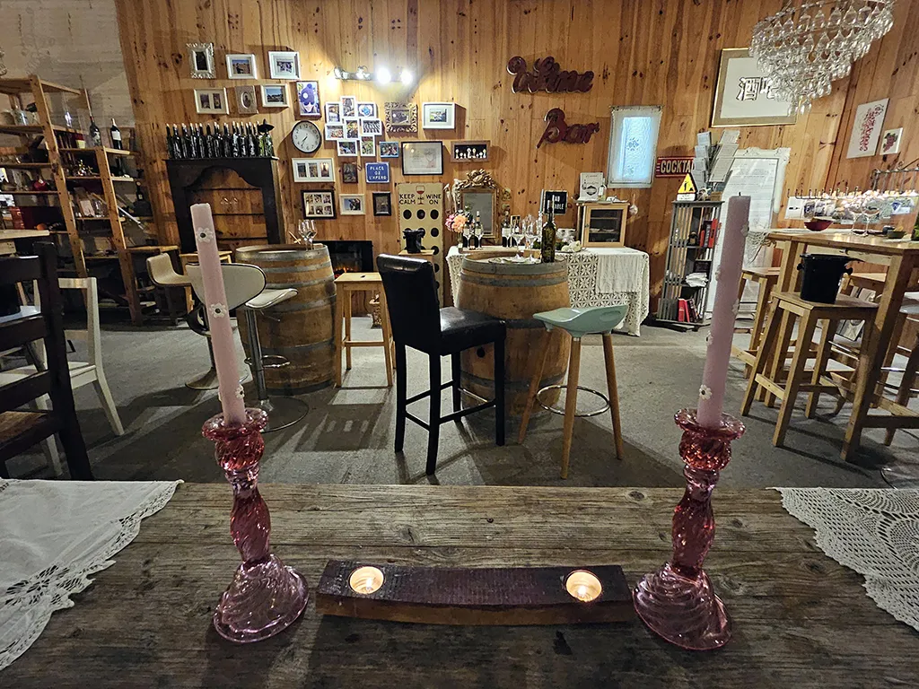 Interior of Château Hourtin-Ducasse in Bordeaux with event decoration: wooden table with pink candelabras, wine barrels, rustic furniture, wooden walls, photographs and decorative objects.