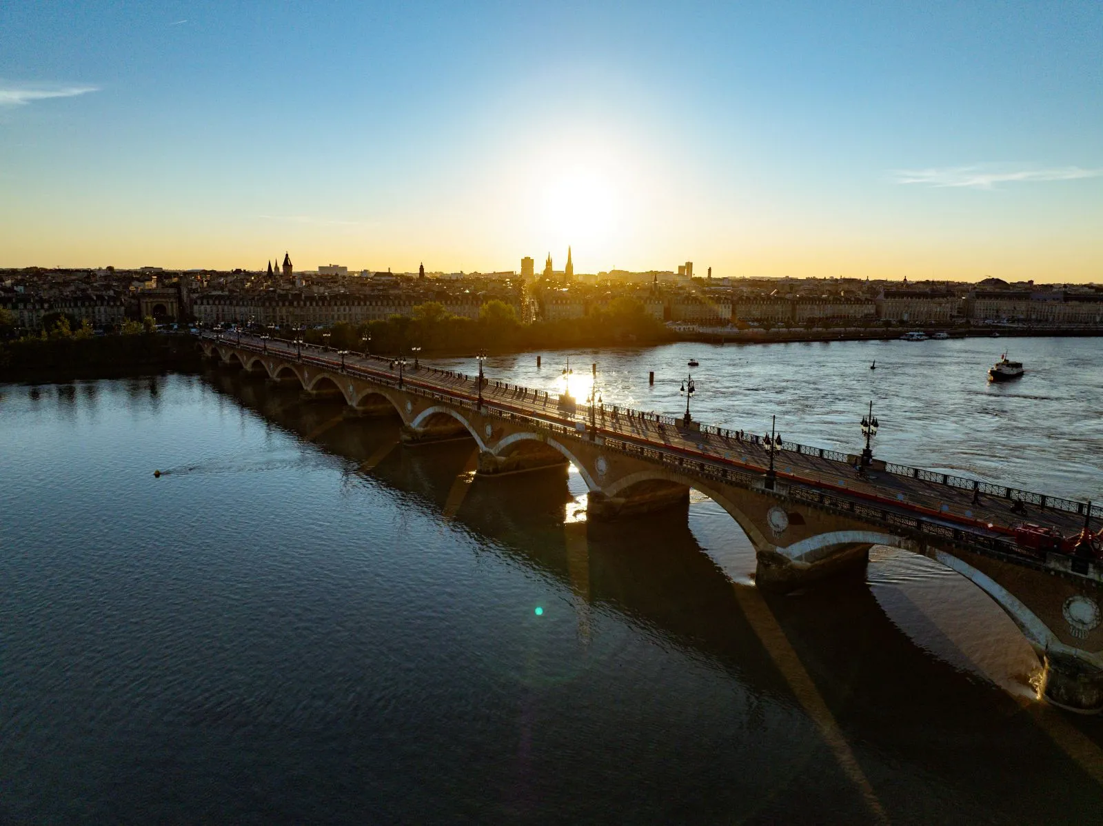 Panoramic view of the Stone Bridge spanning the Garonne River in Bordeaux at sunset, with the cathedral and historic buildings in the background