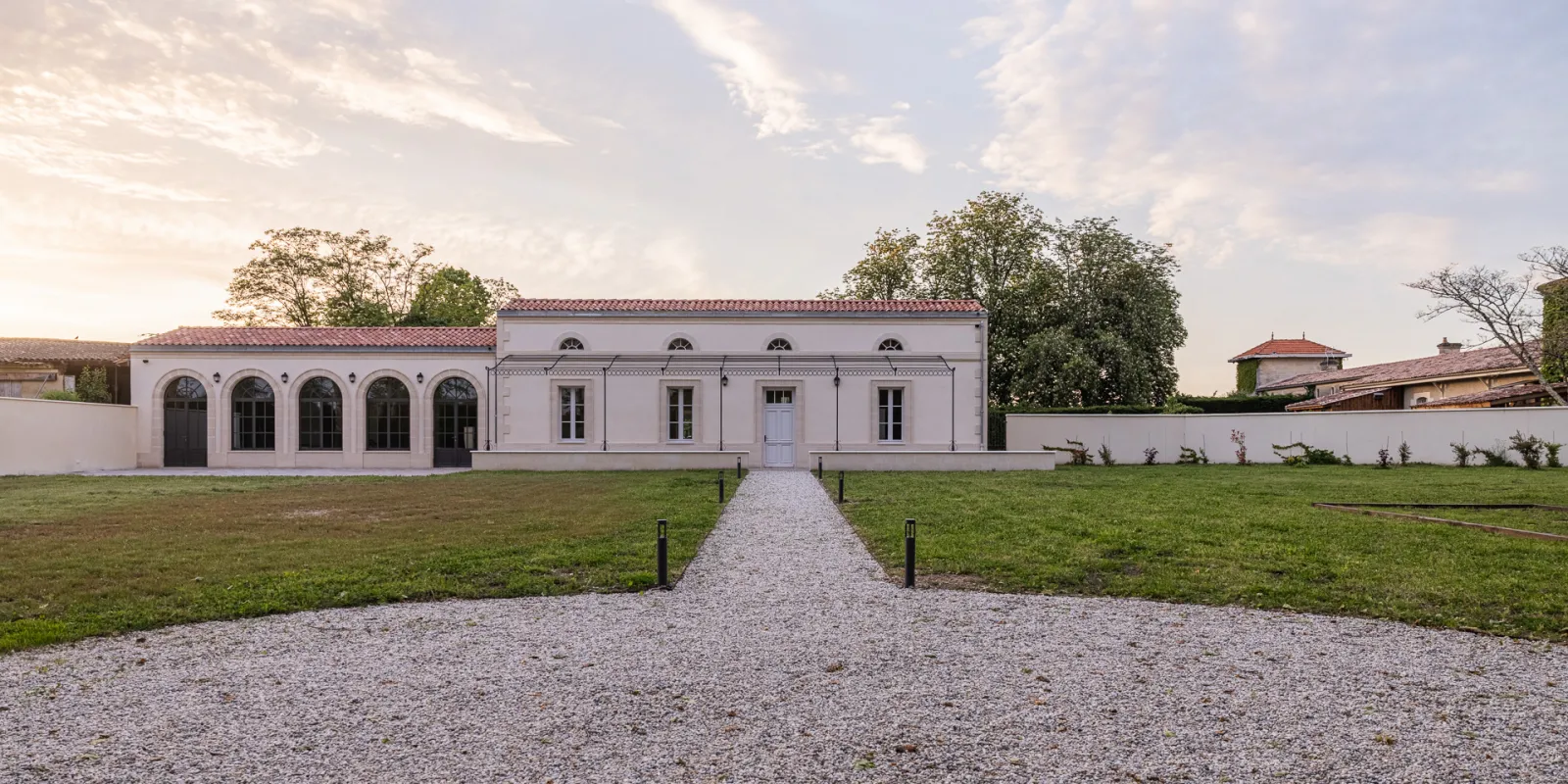 Facade of Château Sénéjac in Bordeaux, white classical building with five arched bays, gravel pathway and green lawn, traditional wine estate architecture.