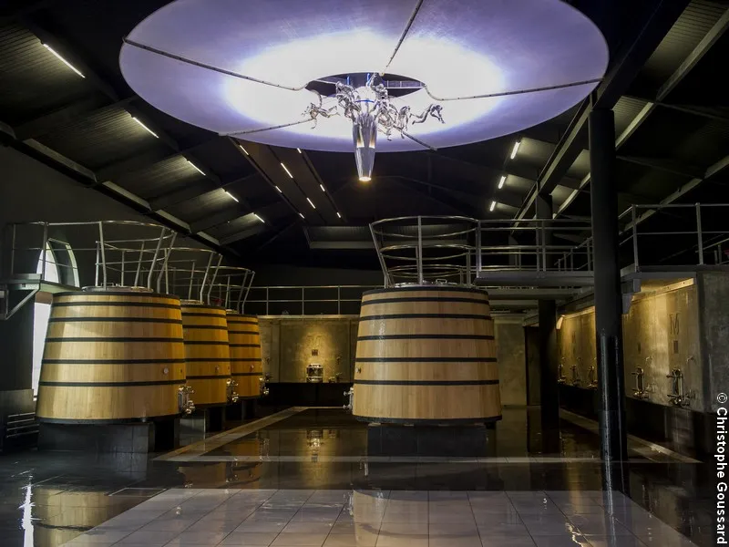 Modern wine cellar interior with large oak barrels arranged under a glowing circular ceiling at Château Malescasse in Bordeaux.