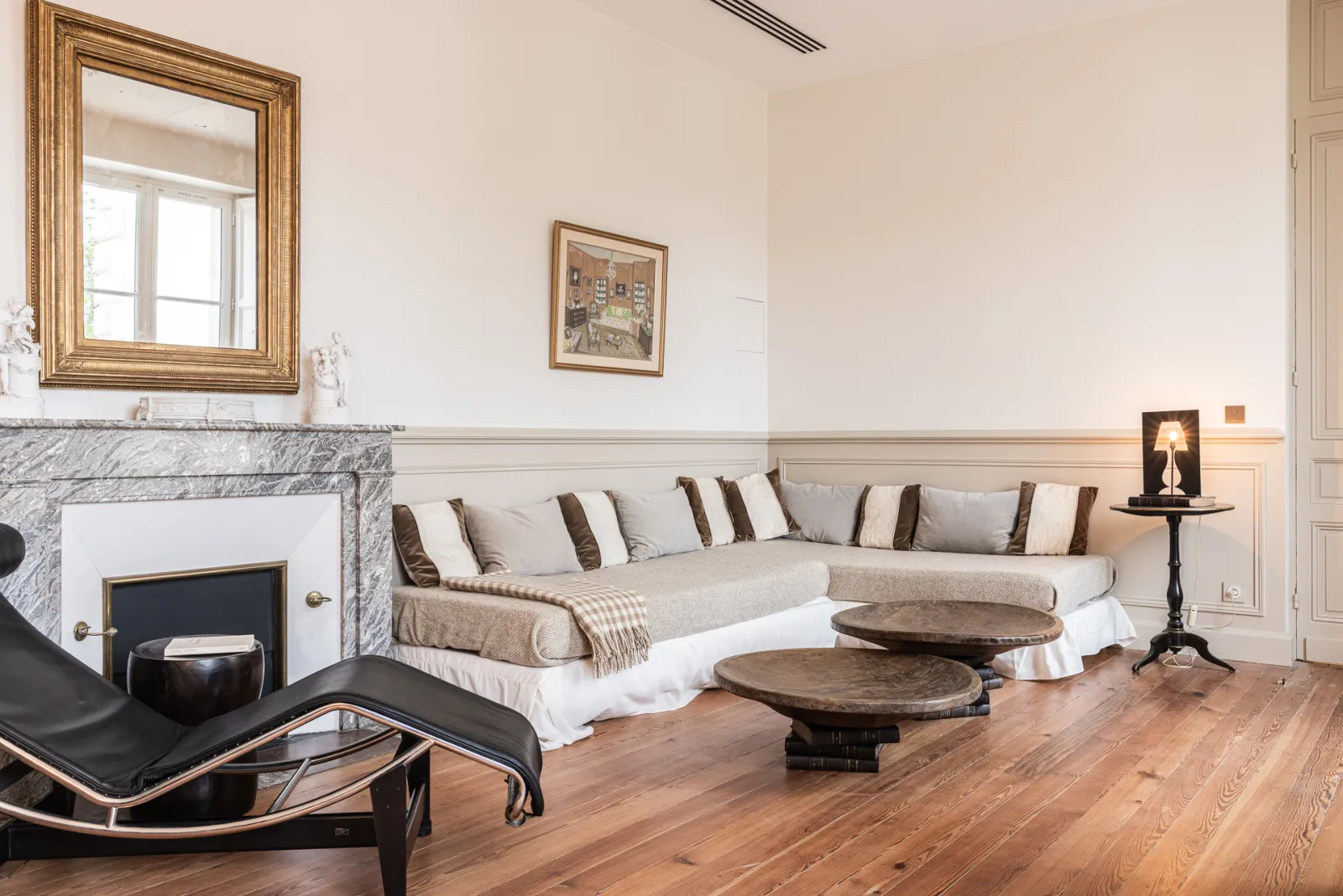 Elegant living room at Château Sénéjac in Bordeaux featuring a marble fireplace, beige striped sofa, wooden flooring, gilt mirror and classic furnishings