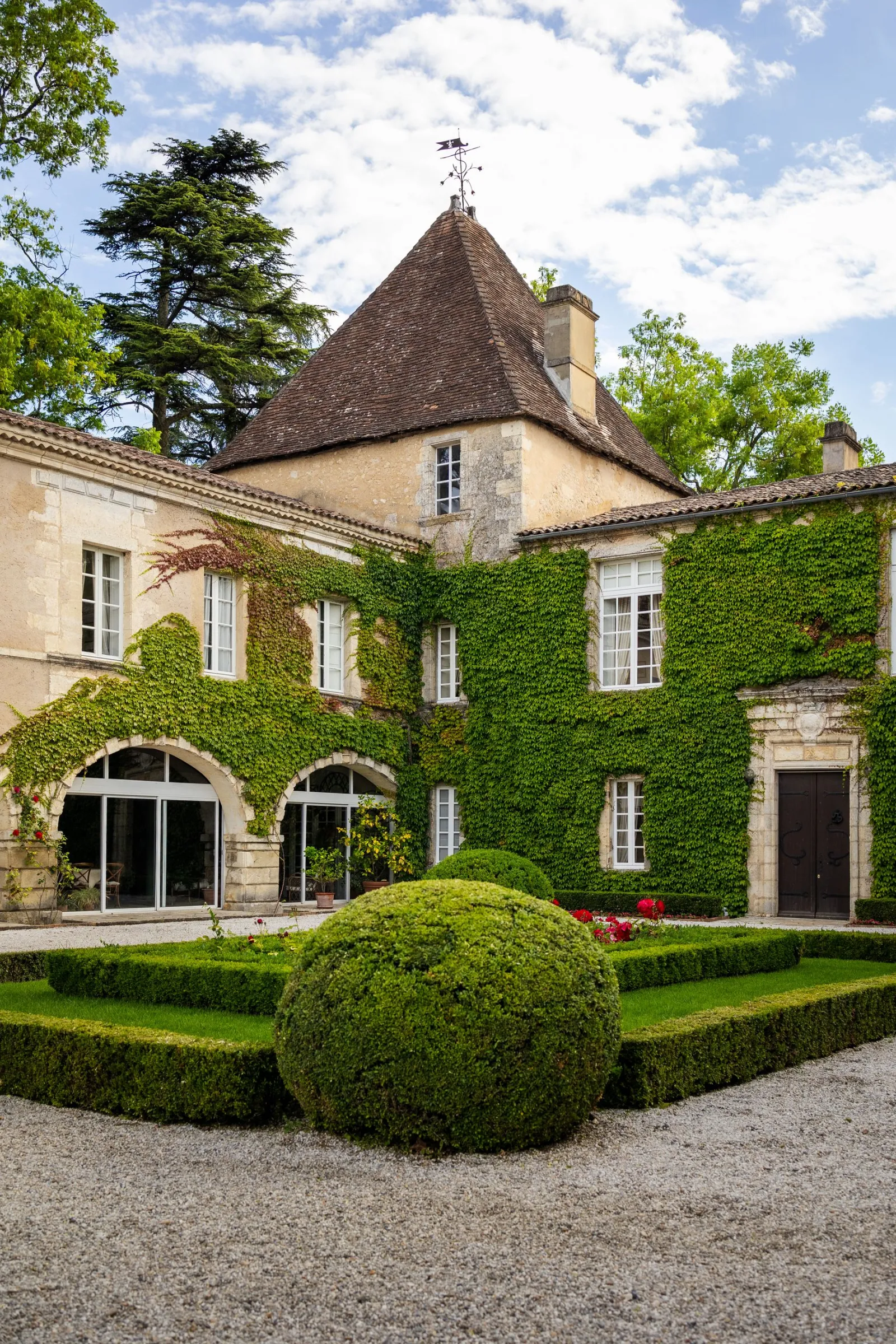 Château Carbonnieux in Bordeaux featuring a conical turret, ivy-covered stone walls, manicured garden with topiary and red flowers