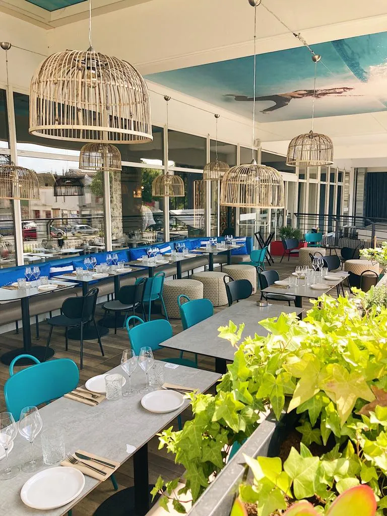 Les Décantés restaurant in Bordeaux featuring modern dining room with black tables, turquoise chairs, wicker pendant lights, large windows and green plants