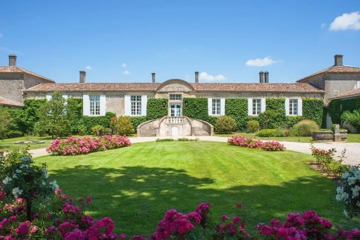 Front view of an elegant Bordeaux mansion at Chambres d'Arche featuring white façade, tiled roof, lush green lawn and vibrant pink and magenta flower beds