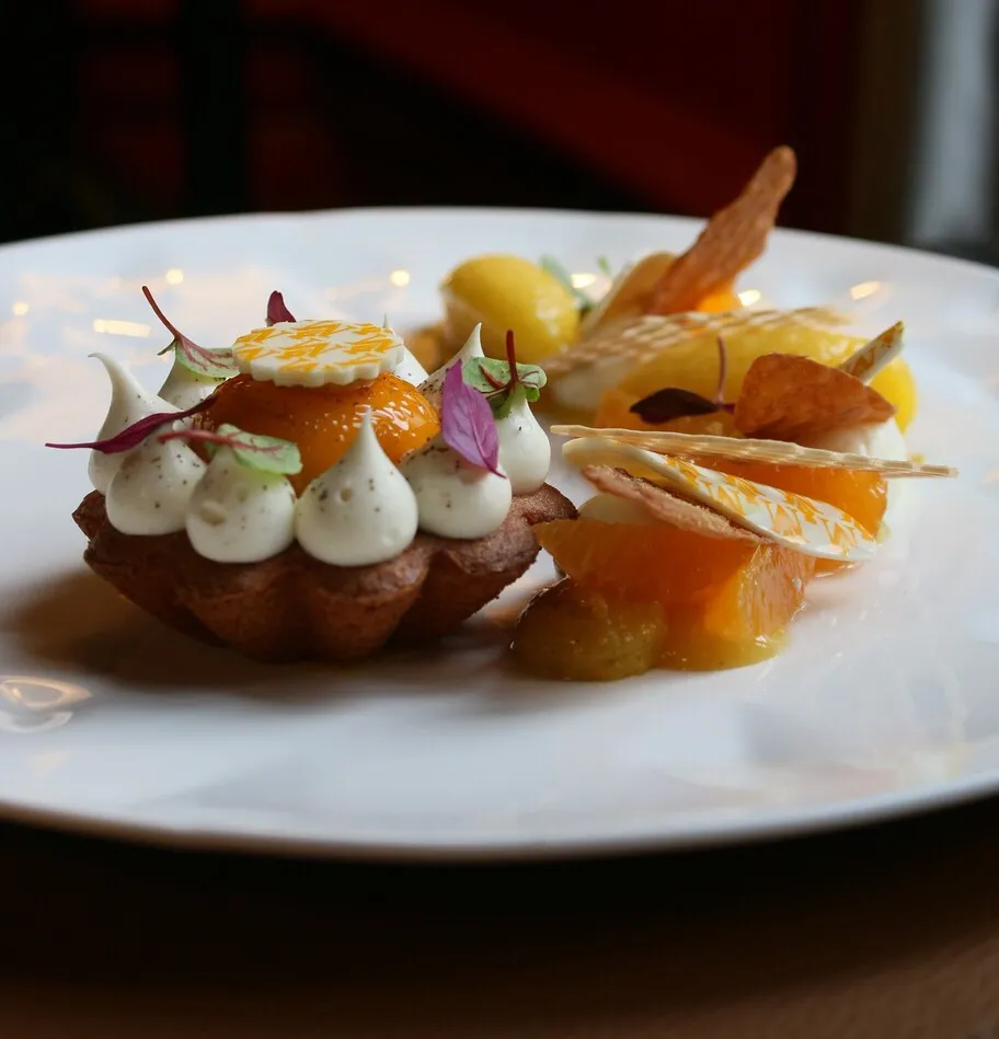 Gourmet plate from Cercle de Montaigne in Bordeaux featuring an elegant dessert with a chocolate base topped with white mousse, garnished with caramelized fruits, purple microgreens and golden edible decorations on a white plate.