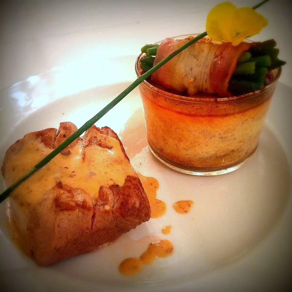 Gourmet dish from La Table de La Chèze in Bordeaux: pan-seared foie gras wrapped in crispy bacon, accompanied by a terrine and garnished with a yellow flower and chive stem, on white plate.