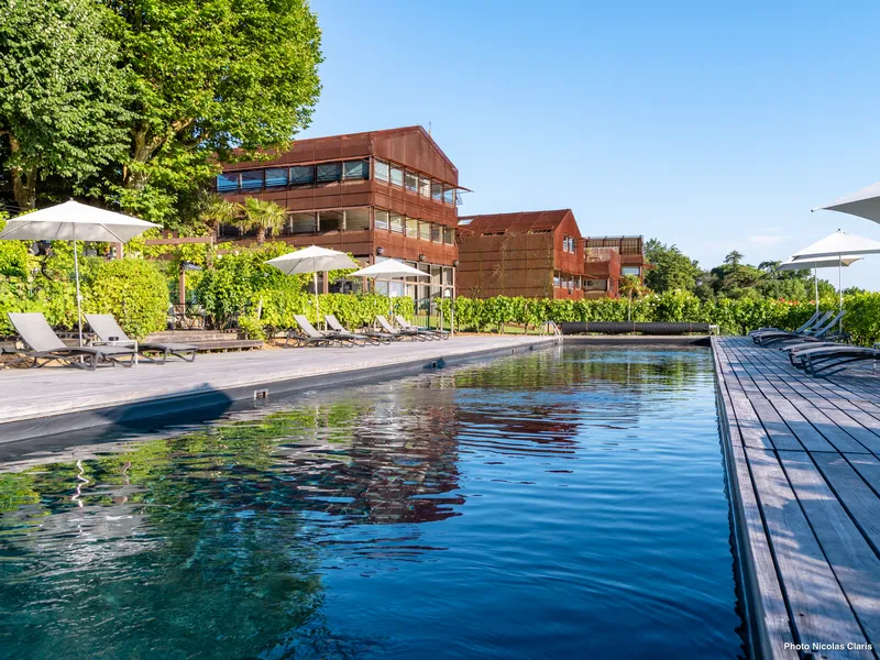 Outdoor swimming pool at Le Saint-James hotel in Bordeaux featuring red brick buildings, sun loungers, umbrellas, and wooden deck