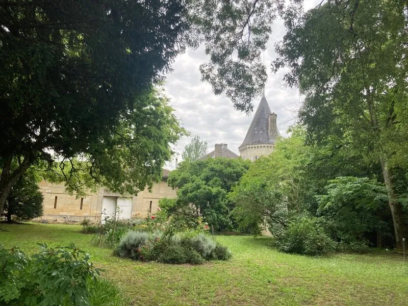 View of Château Gueyrosse in Bordeaux with its characteristic towers, surrounded by lush greenery and century-old trees in its park.