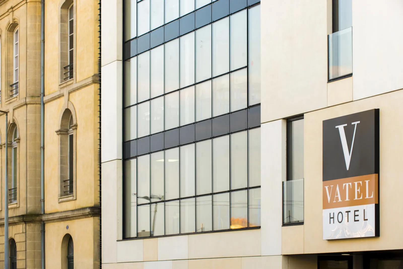 Vatel Hotel facade in Bordeaux, modern building with large glass windows and signage, next to historic yellow stone architecture