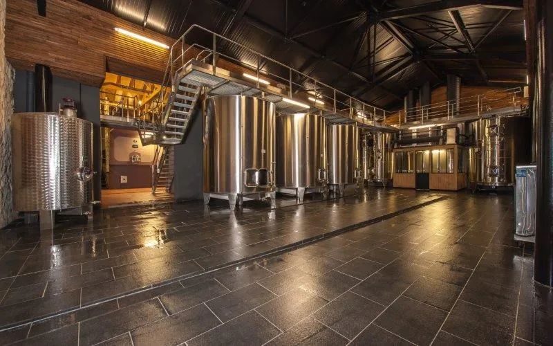 Modern winery interior with stainless steel fermentation tanks, polished tiled floor and metal staircase at Château de Portets in Bordeaux