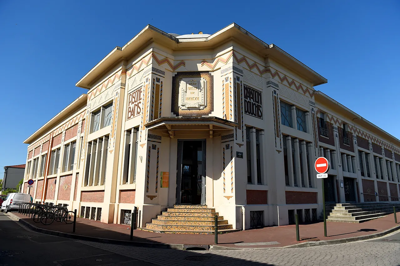 Facade of Les Bains municipal swimming pool in Bordeaux, Art Deco building with geometric brick and white stone details, central entrance with clock.