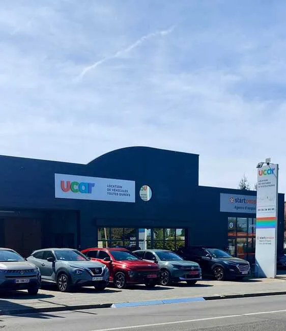 UCAR car dealership in Bordeaux displaying multiple used vehicles in front of the showroom under a partly cloudy sky