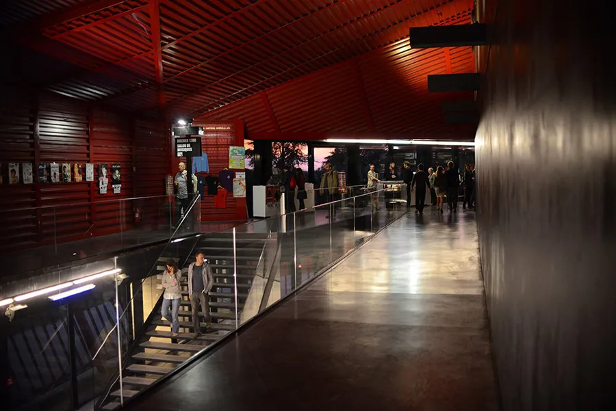 Modern interior of Rocher de Palmer in Cenon featuring red walls, metal stairs, and visitors moving through the exhibition space.