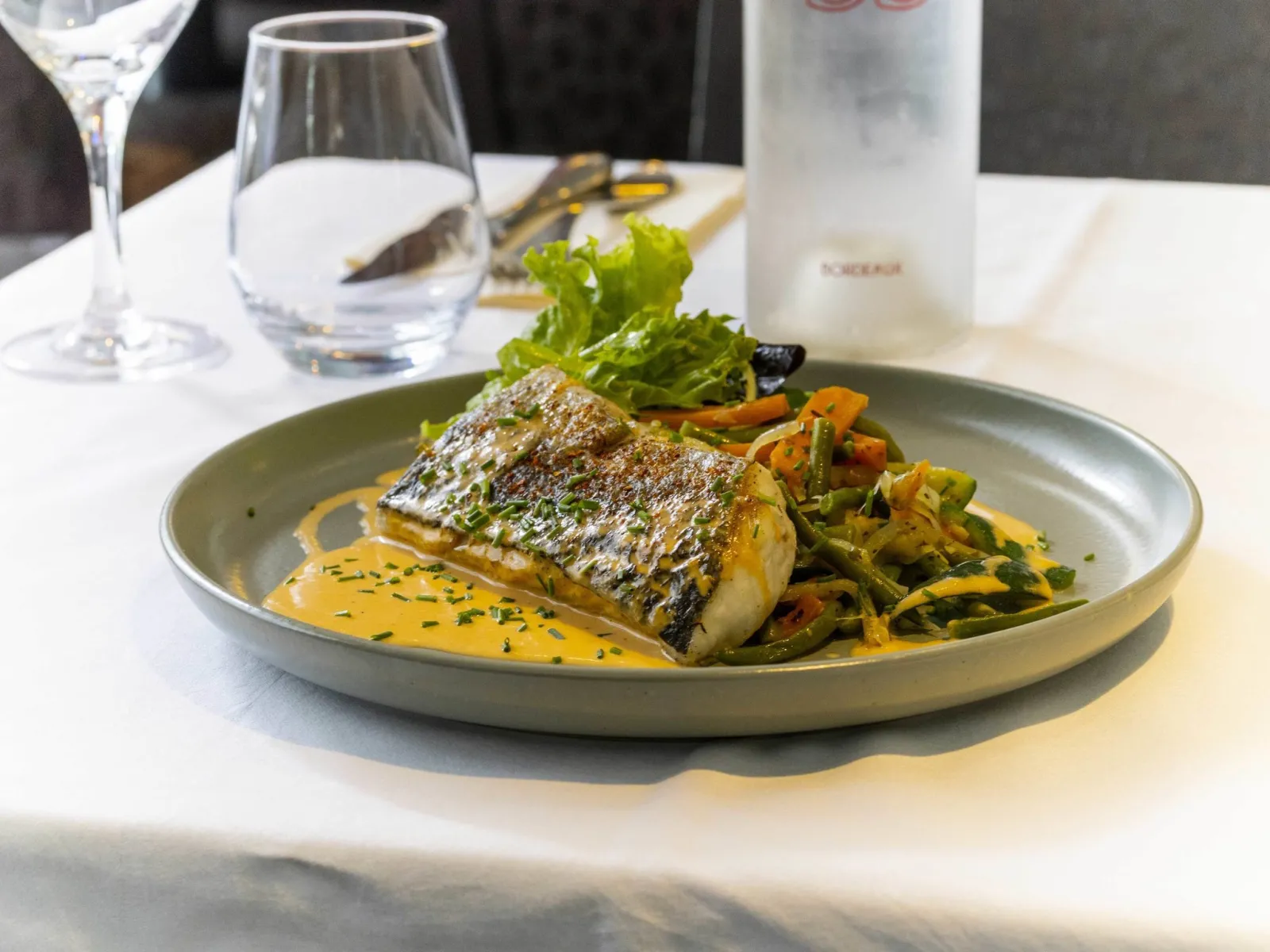 Grilled white fish fillet with crispy skin, yellow sauce, sautéed vegetables and salad on a plate in a fine dining restaurant at Bordeaux Lakeside