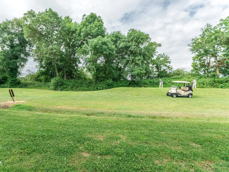 Golf course view with golf cart, lush green trees in the background and cloudy sky at Golf de Margaux near Bordeaux