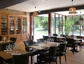Elegant dining room at Château Léognan featuring black tables, gray chairs, light wood cabinetry, and floor-to-ceiling windows overlooking the grounds.