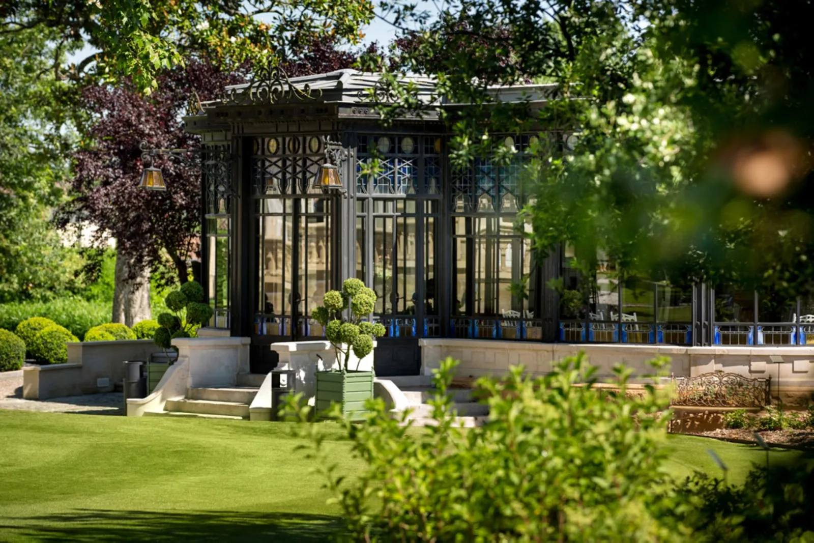 Art Deco glass pavilion of Château Pape Clément in Bordeaux, surrounded by manicured gardens, lawn, and lush green vegetation
