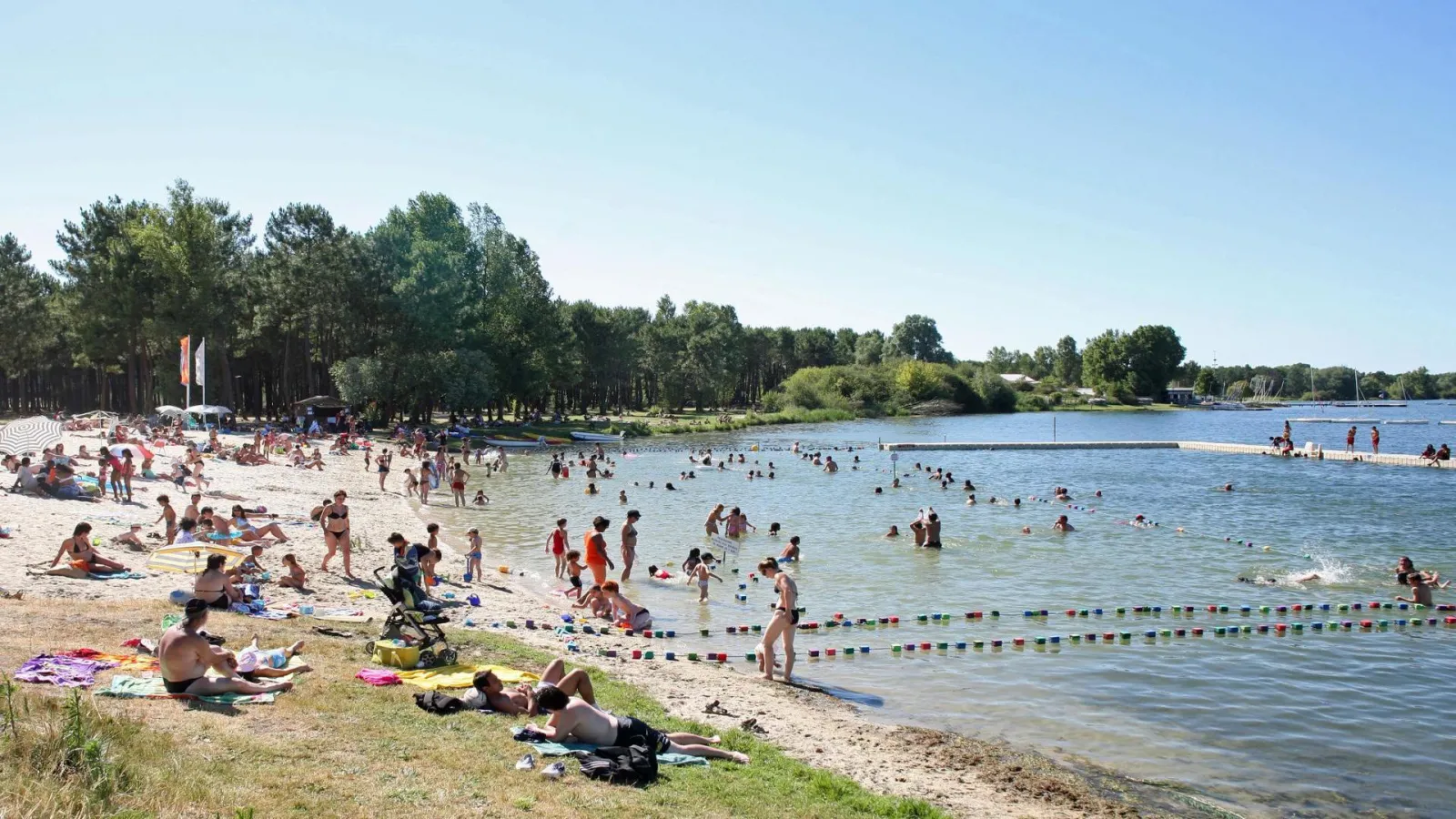 Bordeaux Lake Beach with swimmers, sandy beach, relaxation areas and calm water surrounded by trees