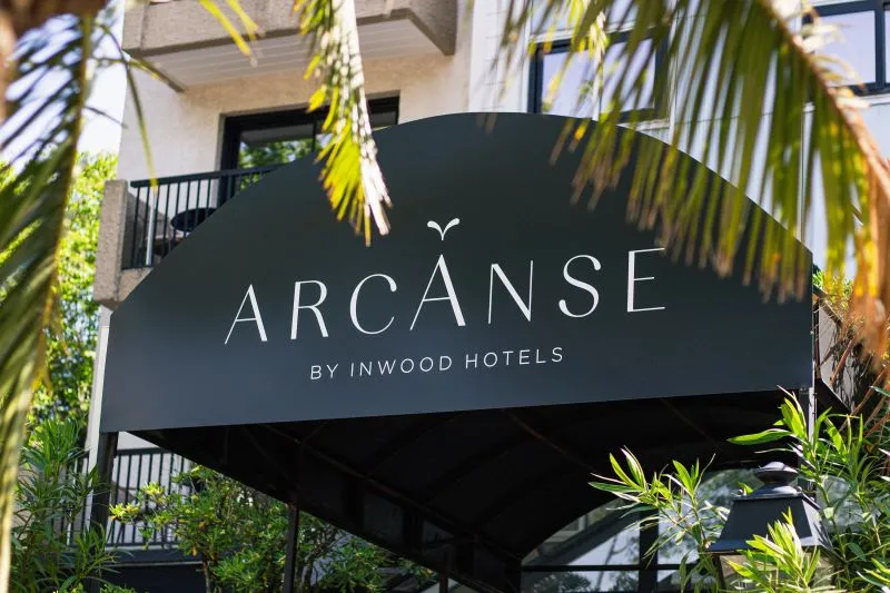 Black Arcanse by Inwood Hotels sign in Bordeaux, surrounded by tropical foliage with white building behind