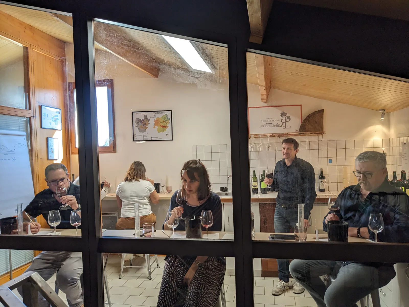 Visitors enjoying a wine tasting in the cellar of Château La Rose Perrière in Bordeaux, seated around a table with wine glasses and bottles.