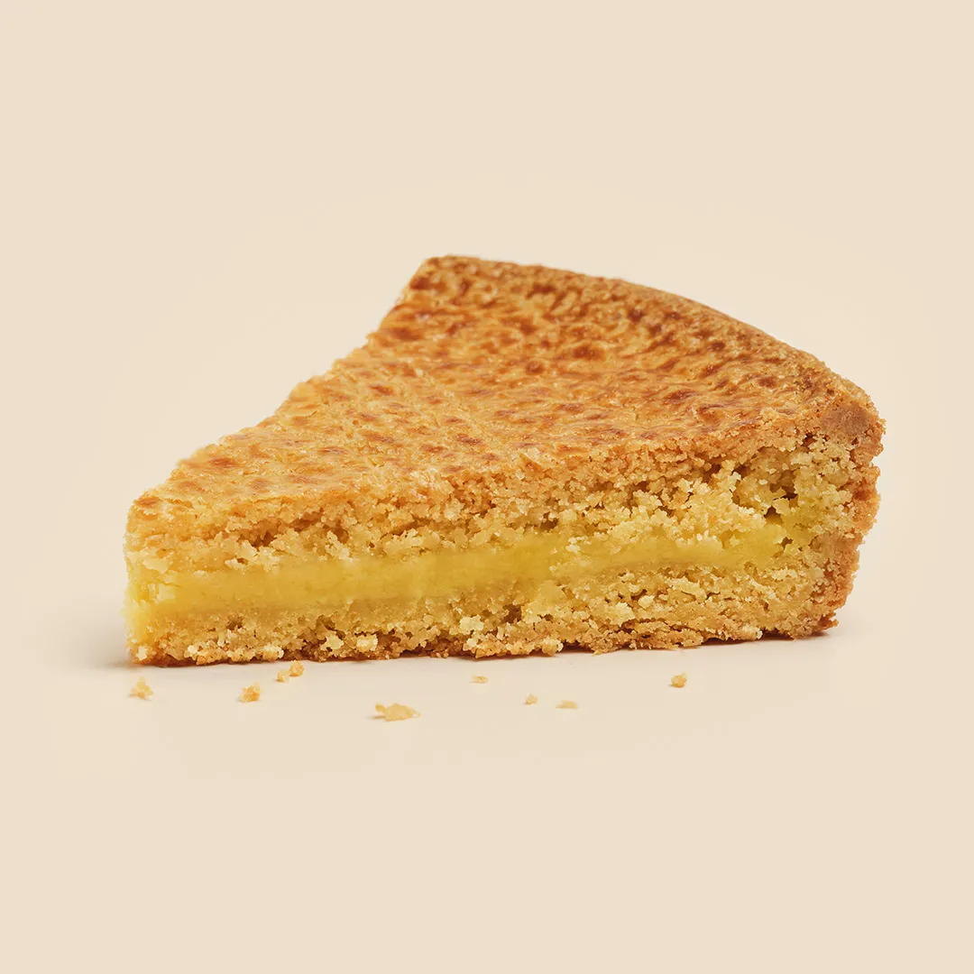 Slice of almond financier cake with a soft pale yellow center on a beige background