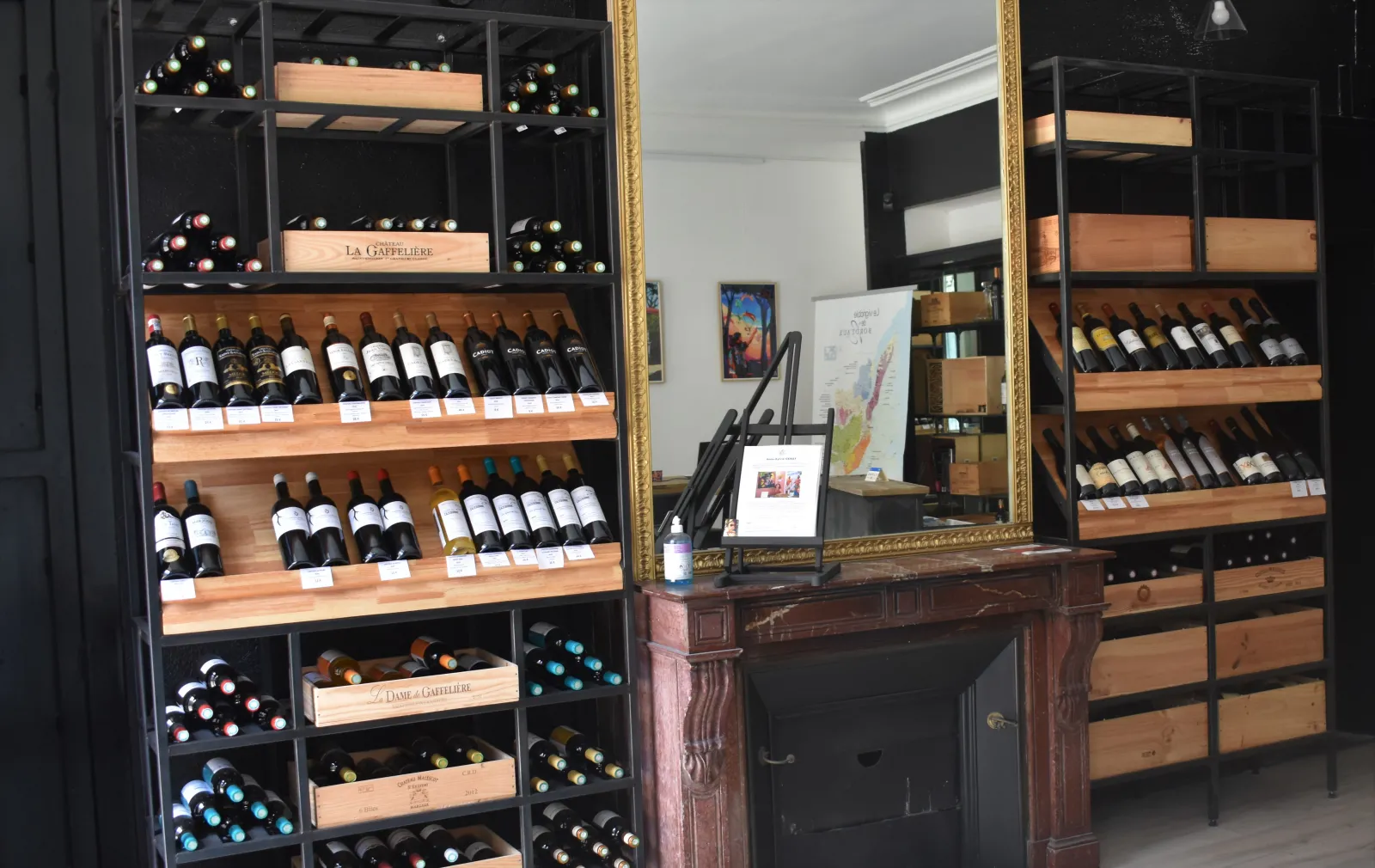 Interior of a Bordeaux wine shop featuring wooden shelves displaying wine bottles, an ornate wooden counter with a gilded mirror, and storage display cases.
