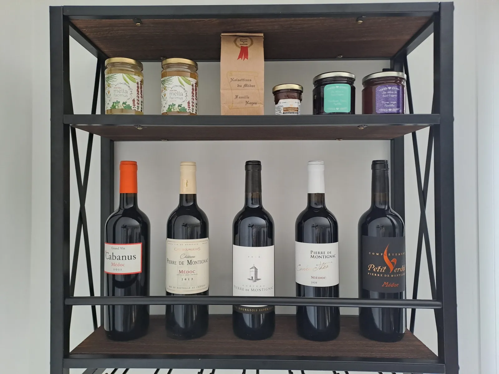 Black metal and wood shelving unit displaying five Bordeaux wine bottles on the lower shelf and beauty products and accessories on the upper shelf at the Anthocyane guest house of Château Pierre de Montignac.