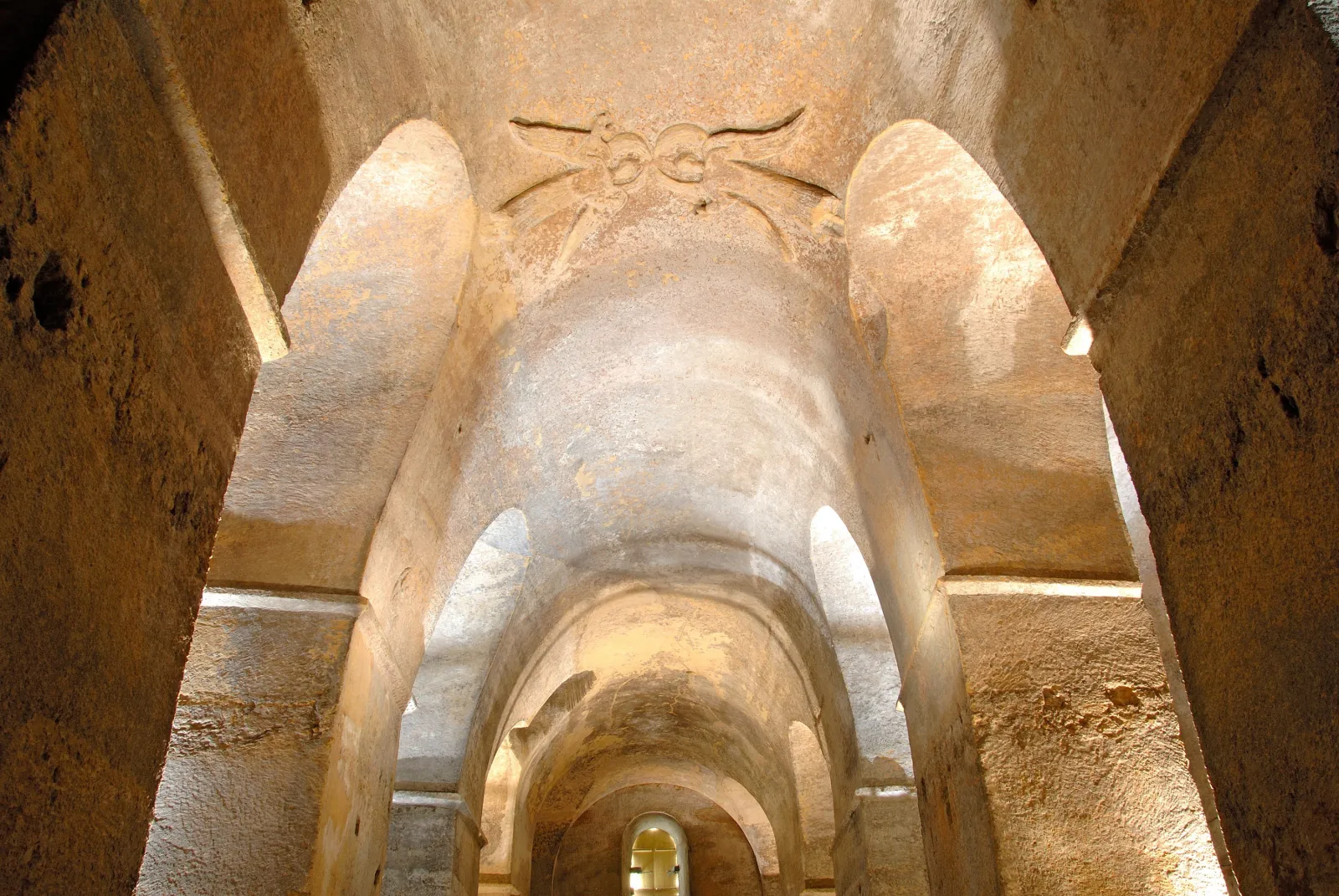 Underground vaulted gallery in Saint-Émilion with stone arches and sculpted ceiling decoration, lit by natural light.