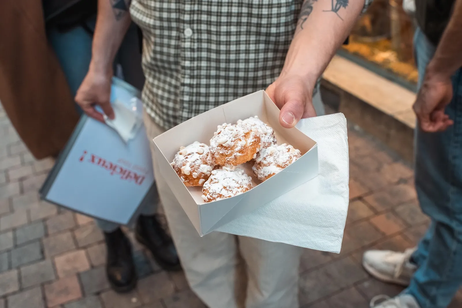 A person holding a white box with powdered sugar-coated pastries during a food tour in Bordeaux.