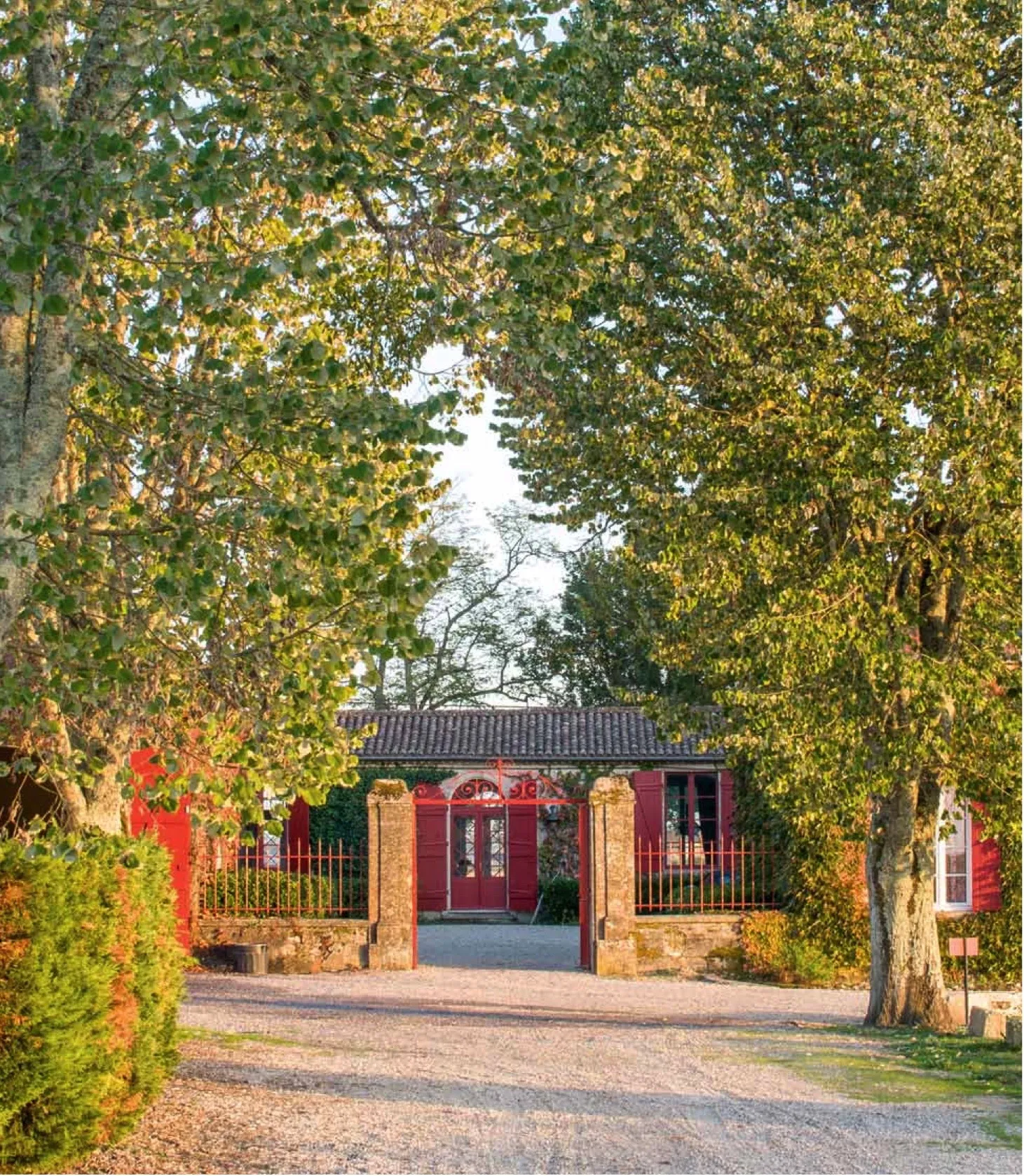 Entrance gate of Château Sigalas Rabaud in Bordeaux featuring a red door, stone pillars, and tree-lined driveway with golden autumn foliage.