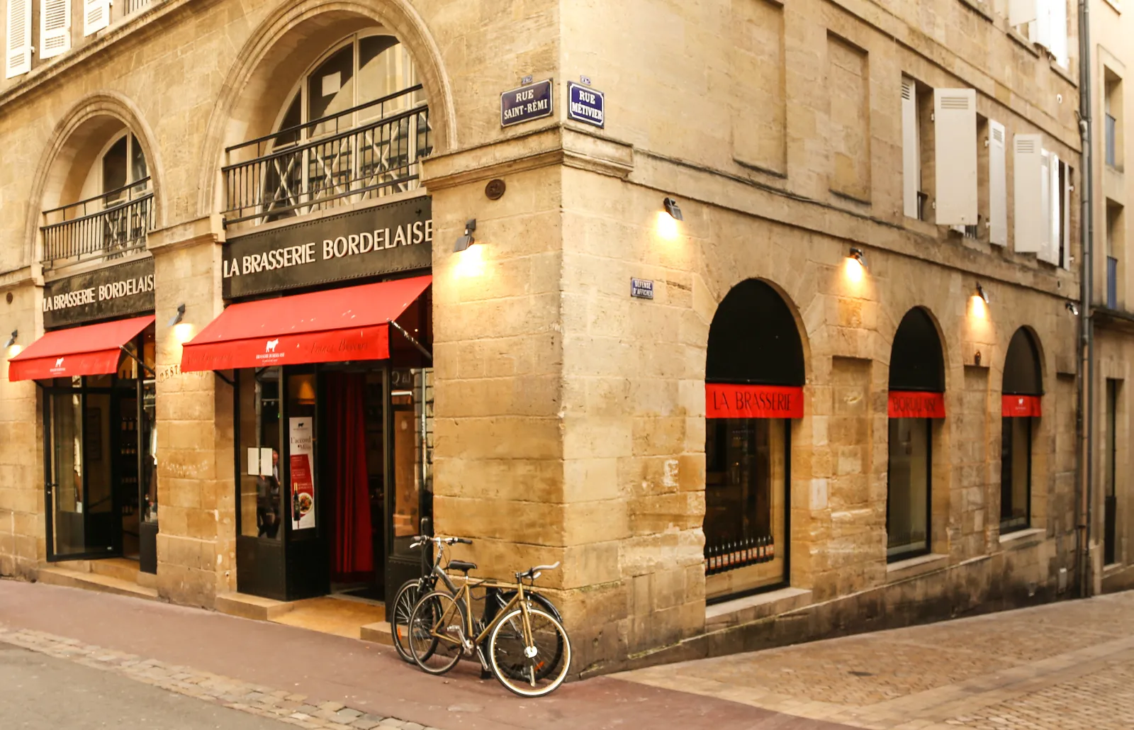 Storefront of Brasserie Bordelaise in Bordeaux, featuring red awnings, arched windows and a bicycle parked in front on Rue Saint-Rémi