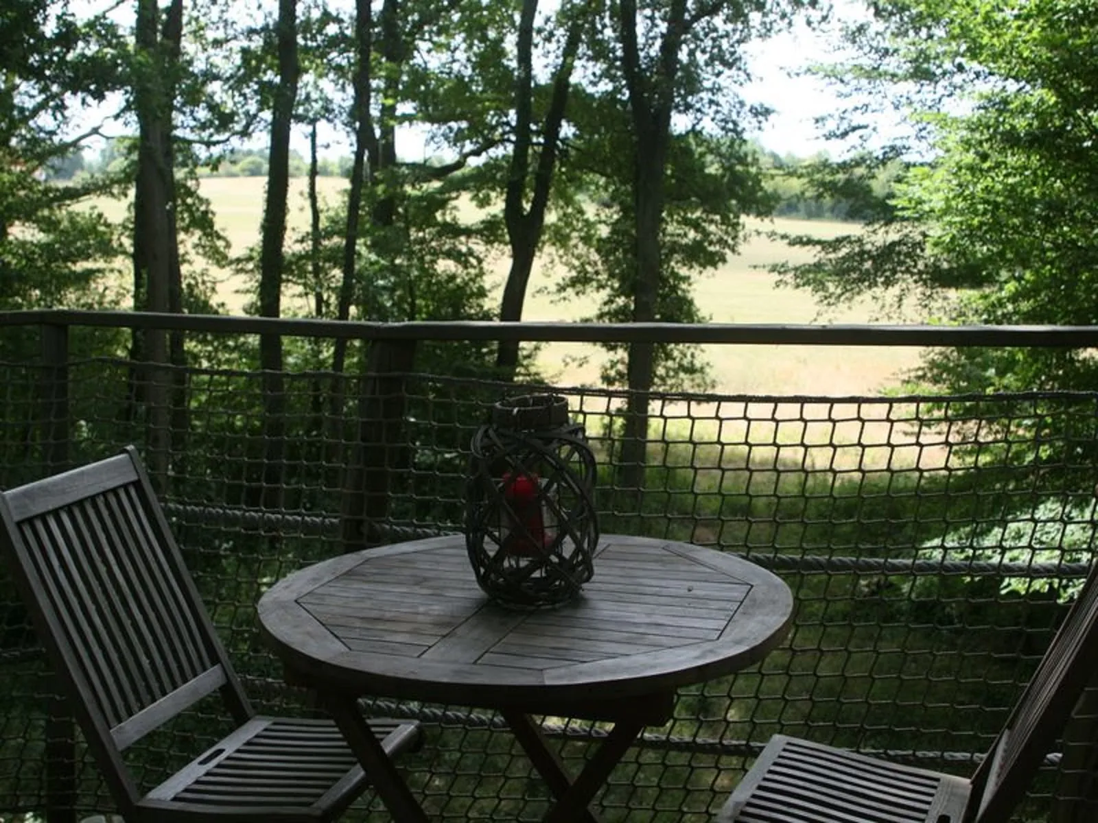 Deck terrace overlooking fields and river with two lounge chairs and round table, surrounded by dense forest at Cabanes de la Romaningue near Bordeaux