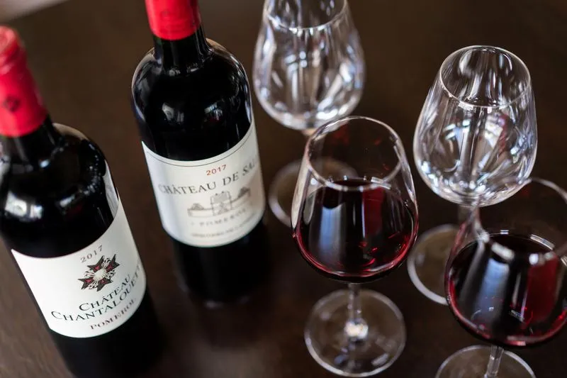 Wine tasting of Château de Sales 2017 Bordeaux wines: two bottles and three glasses containing red wine on a dark surface.