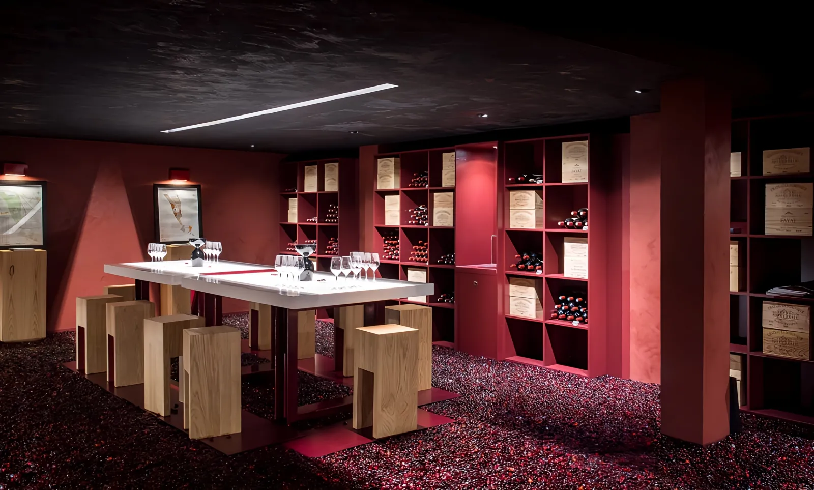 Modern wine tasting room at Château La Dominique in Bordeaux featuring burgundy red walls, white counter, light wood stools, wine bottle storage shelves, and red stone flooring.