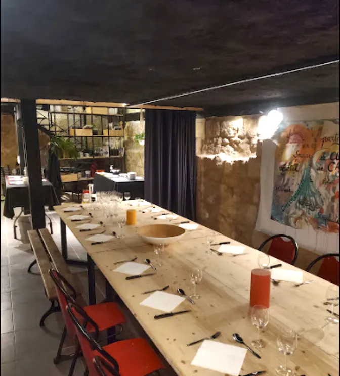 Modern restaurant dining room with a long wooden table set for a meal, red chairs, black cutlery, water glasses, contemporary wall art and ambient lighting in Bordeaux.