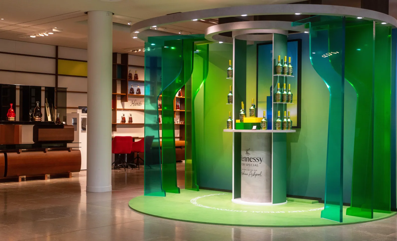 Modern exhibition space of the Hennessy tour in Bordeaux featuring a circular display with illuminated green panels showcasing Hennessy cognac bottles and a large white bottle in the background.