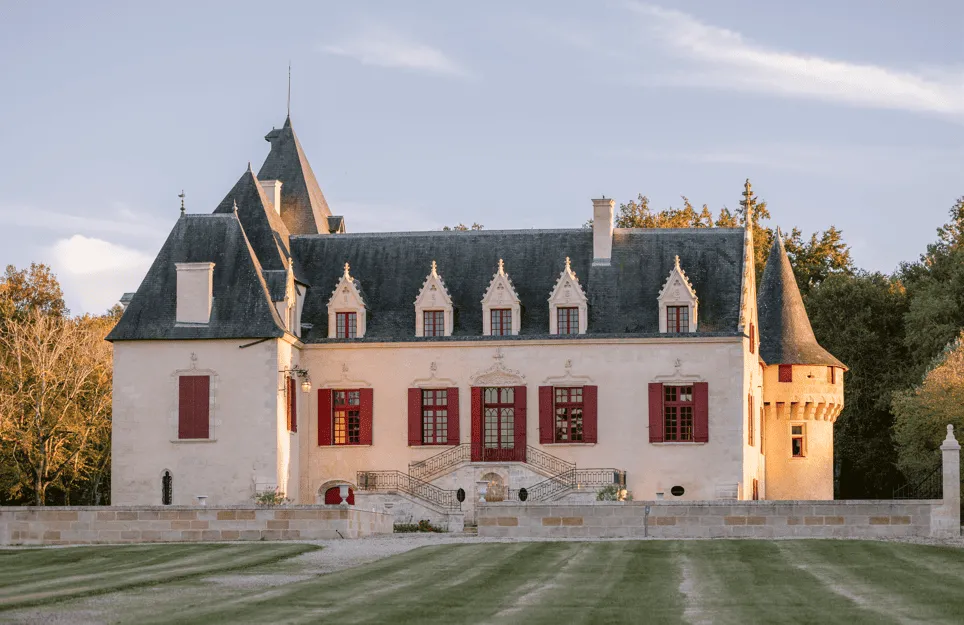 Château Olivier in Bordeaux, a white manor house with slate roofs, pointed towers and red doors, surrounded by a green park.