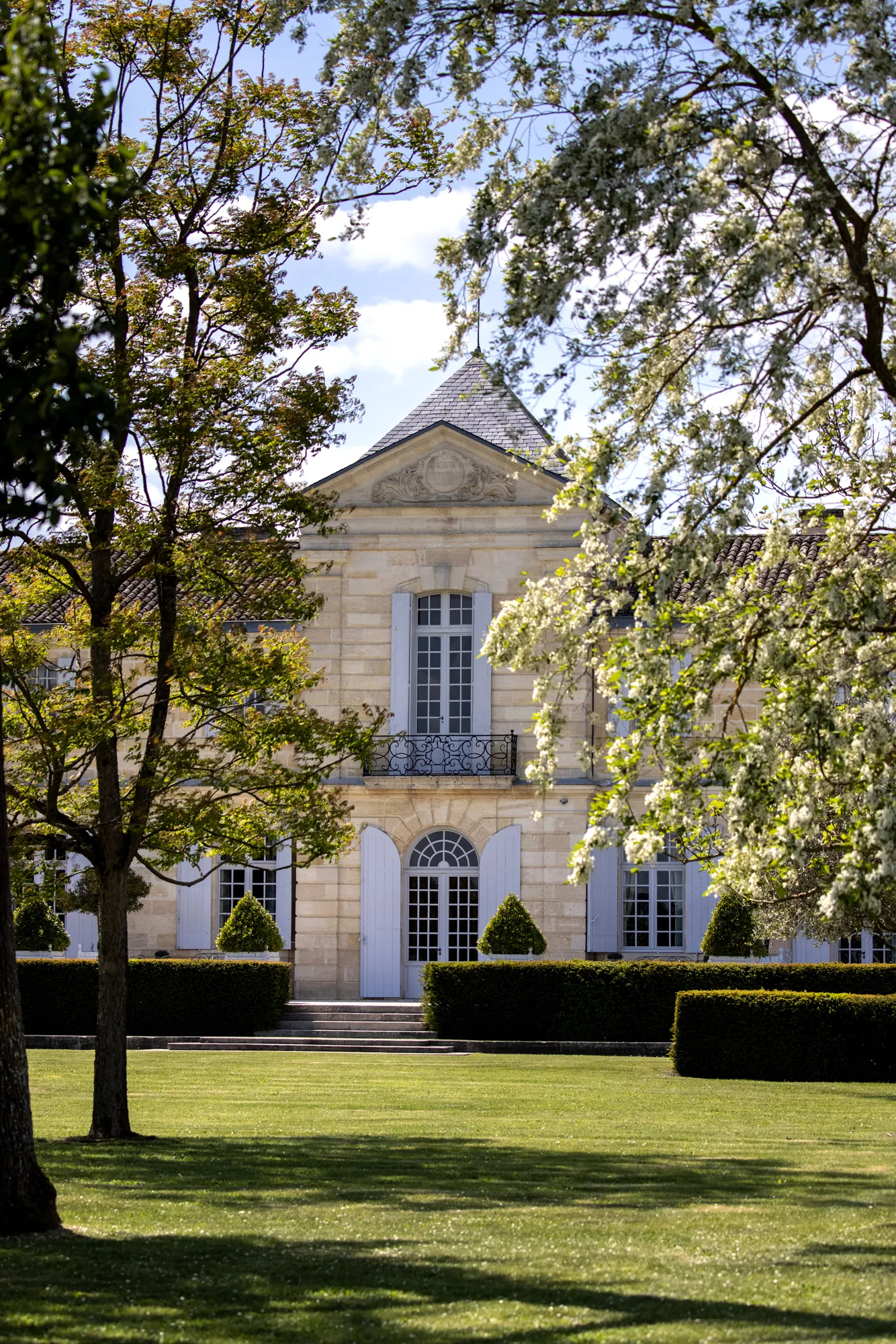 Château du Tertre in Bordeaux, an elegant classical stone mansion with white ashlar facade, arched windows, slate roof, surrounded by mature trees and landscaped gardens.