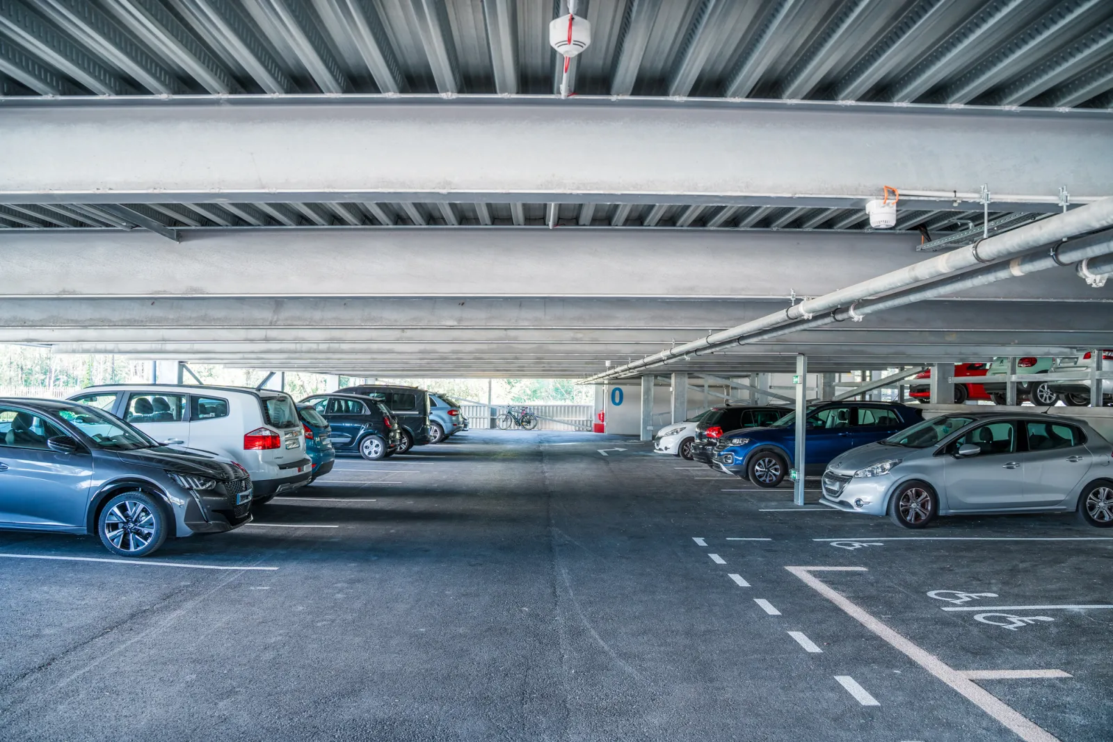 Underground covered parking lot with multiple parked vehicles, natural lighting and modern infrastructure at Holiday Inn Bordeaux Mérignac