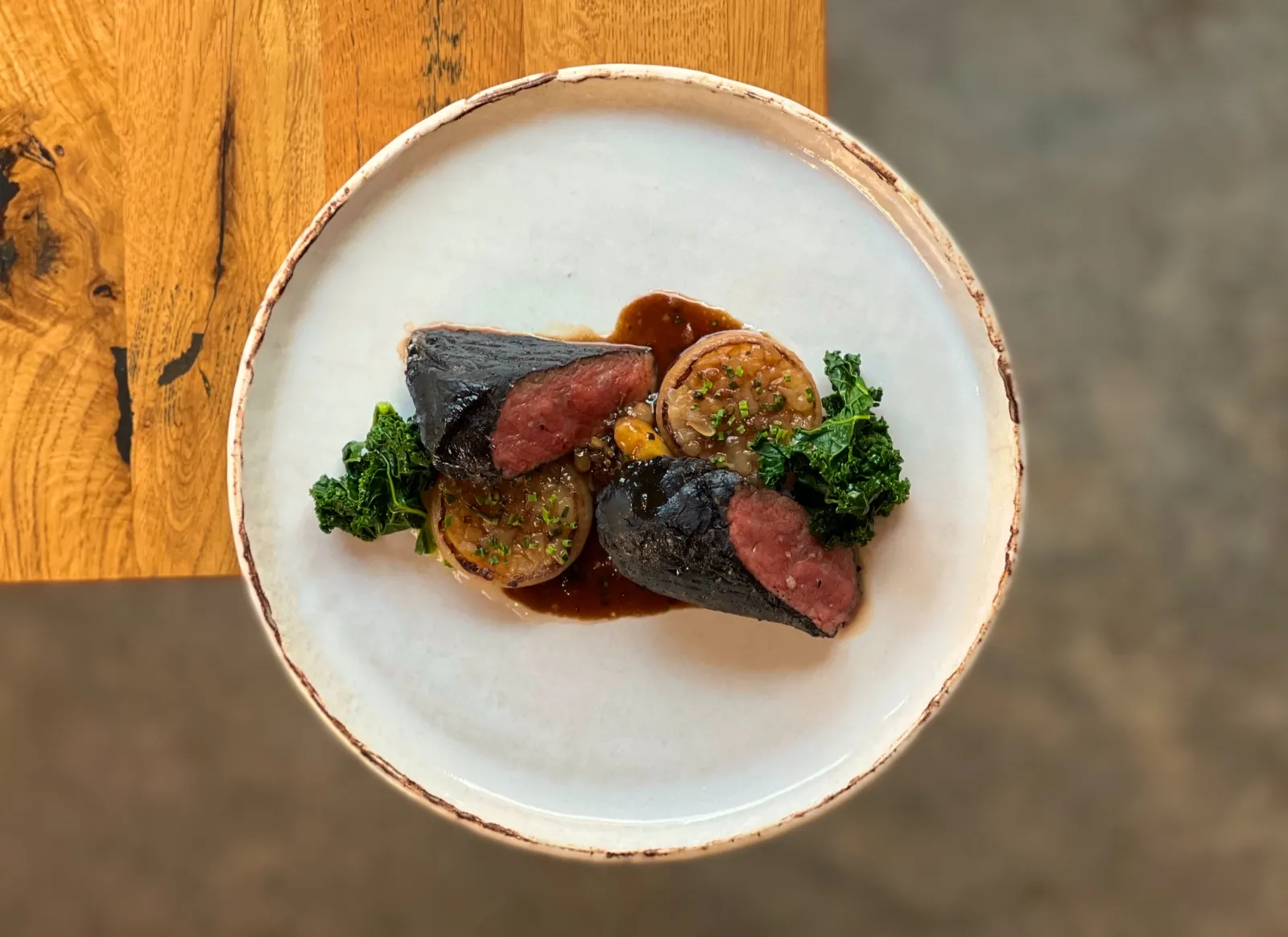Fine dining plate featuring rare sliced meat accompanied by grilled vegetables, kale, and sauce, served at an upscale Bordeaux restaurant