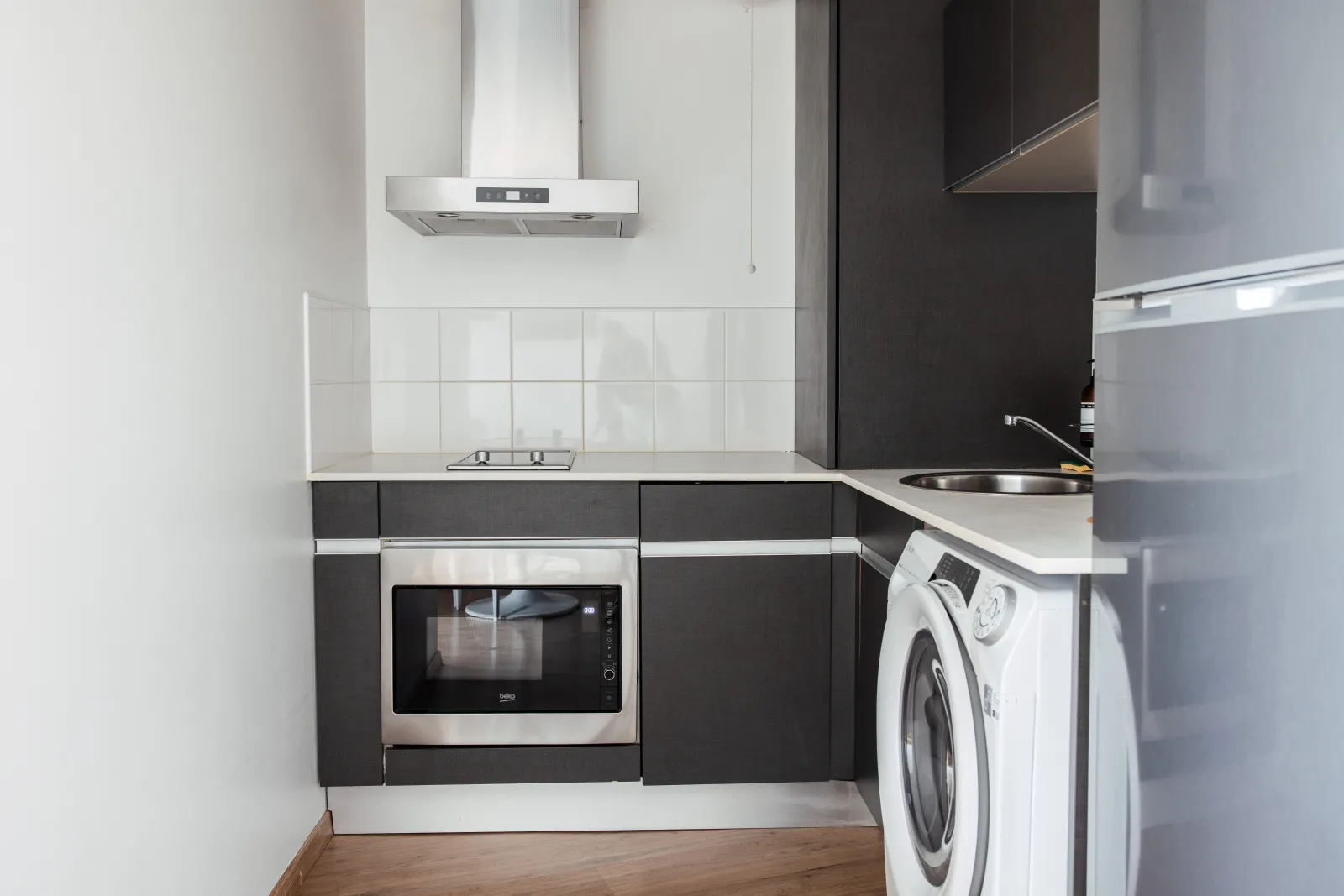 Modern kitchen in a serviced apartment featuring black and white cabinetry, built-in oven, range hood, white countertop, and laundry space with washing machine.