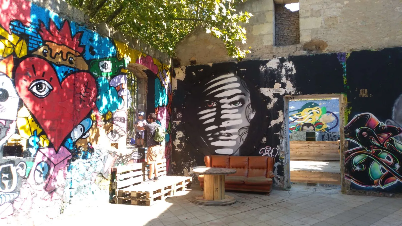 Vibrant urban space featuring colorful street art murals on walls, a red sofa, artistic installations and greenery at Darwin Caserne Niel, Bordeaux