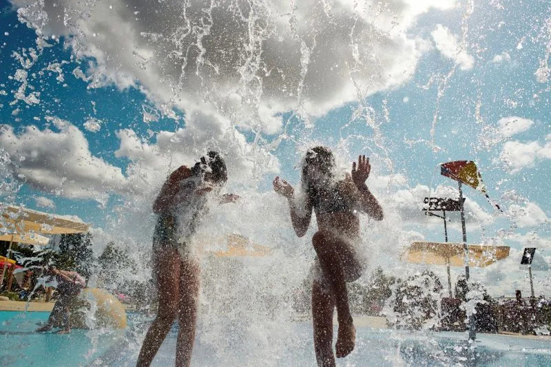 Two children enjoying a water cascade at La Calinésie aquatic center in Libournais, Bordeaux, on a sunny day.