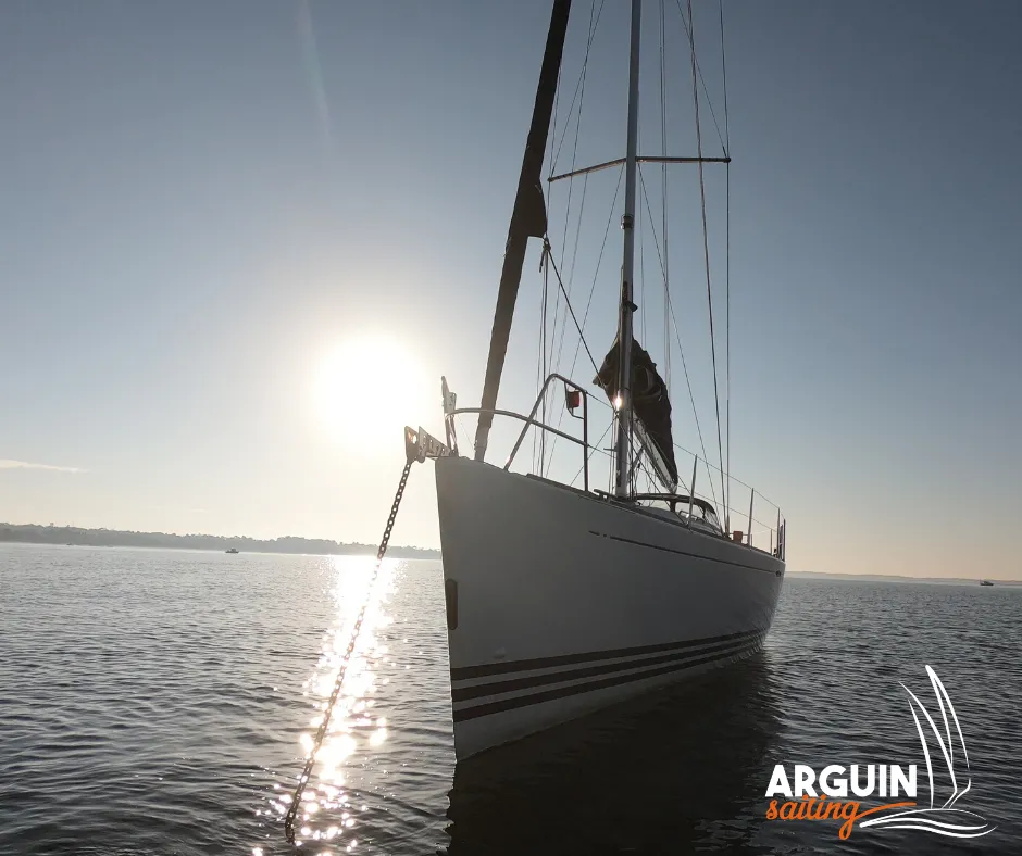 White sailing yacht anchored in the Gironde estuary near Bordeaux, front view with sunlight reflecting on the water and sails down