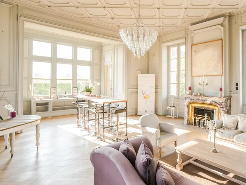 Elegant living room at Château Giscours near Bordeaux featuring classic furniture, golden fireplace, crystal chandelier and large windows overlooking the grounds