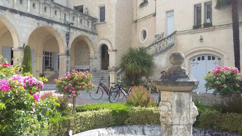 Interior courtyard of a Bordeaux mansion featuring stone arcades, pink flowers, a parked bicycle, and an old fountain