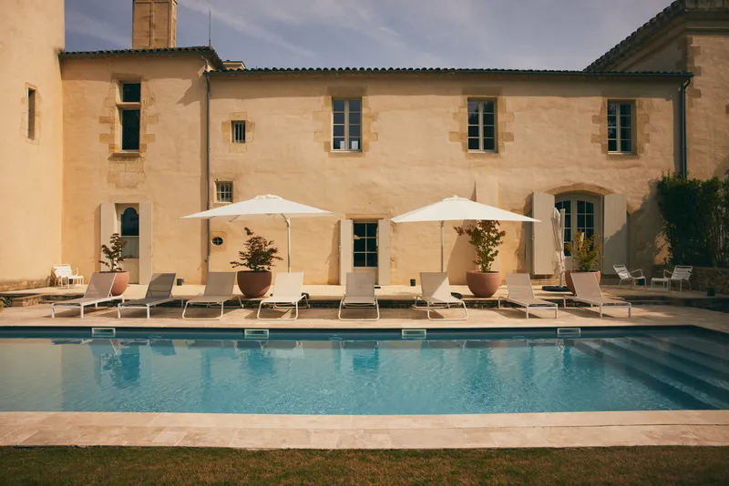 Swimming pool at Château Toulouse Lautrec in Bordeaux featuring white loungers, umbrellas, and stone facade